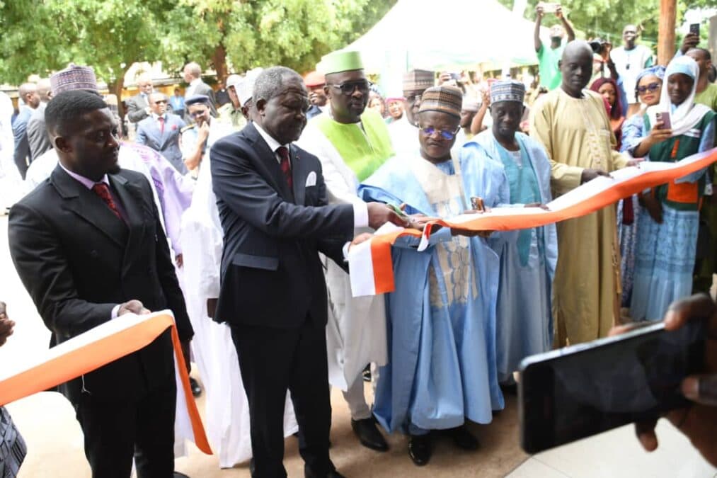 Cliché pris sur le vif montrant la coupure du ruban officiel (orange et blanc) par le Directeur Général, Tchoupou Zéphyrin Blaise, entouré de dignitaires et personnalités locales vêtus de tenues traditionnelles et de costumes, en présence d'invités et de photographes.Cliché pris sur le vif montrant la coupure du ruban officiel (orange et blanc) par le Directeur Général, Tchoupou Zéphyrin Blaise, entouré de dignitaires et personnalités locales vêtus de tenues traditionnelles et de costumes, en présence d'invités et de photographes.