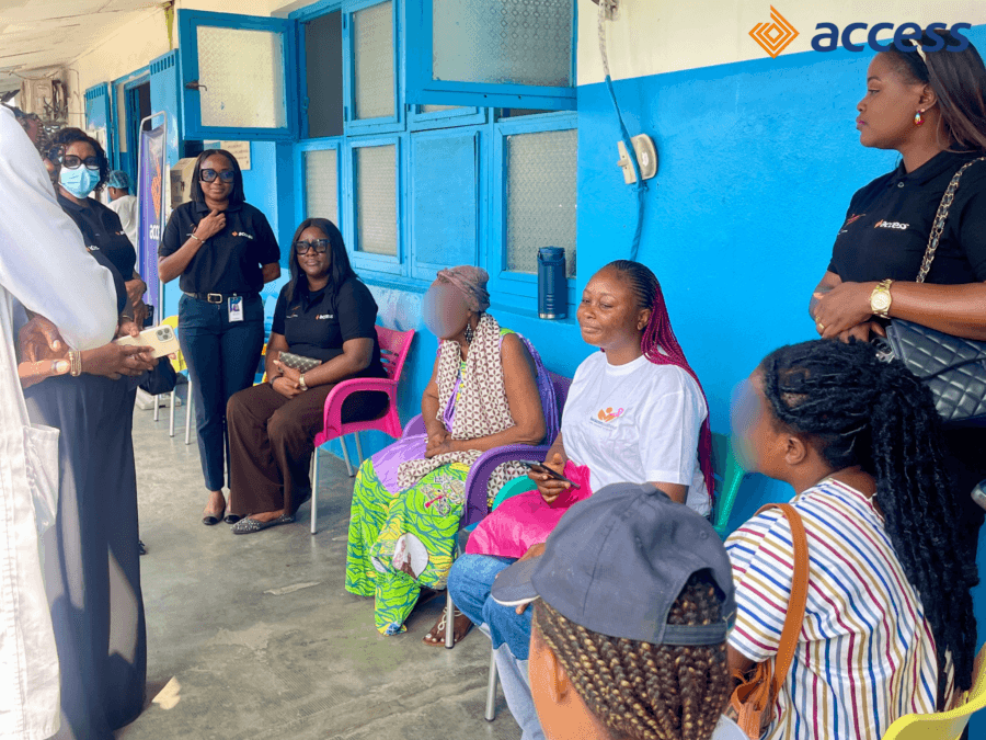 Une vue d'ensemble montrant la délégation d'Access Bank Cameroon (portant des hauts noirs de l'Initiative W) ainsi que les équipes de BeaconPasteur réunies dans la cour intérieure/couloir de l'hôpital. Elles sont assises et debout aux côtés de patientes atteintes de cancer pour échanger avec elles, leur témoigner leur soutien moral et discuter du déroulement des soins avec le personnel médical.