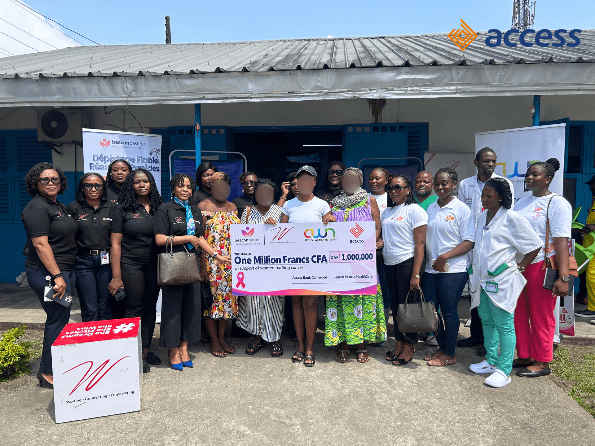 Photo de groupe réunissant la délégation d'Access Bank Cameroon, les représentantes d'Access Women Network (AWN) et de l'Initiative W, le personnel du Laboratoire BeaconPasteur, les médecins de l'hôpital et les patientes bénéficiaires. Au centre, ils tiennent un grand chèque factice d'une valeur de 1 000 000 XAF (Un million de Francs CFA) destiné à alléger les charges médicales liées au traitement du cancer du sein.