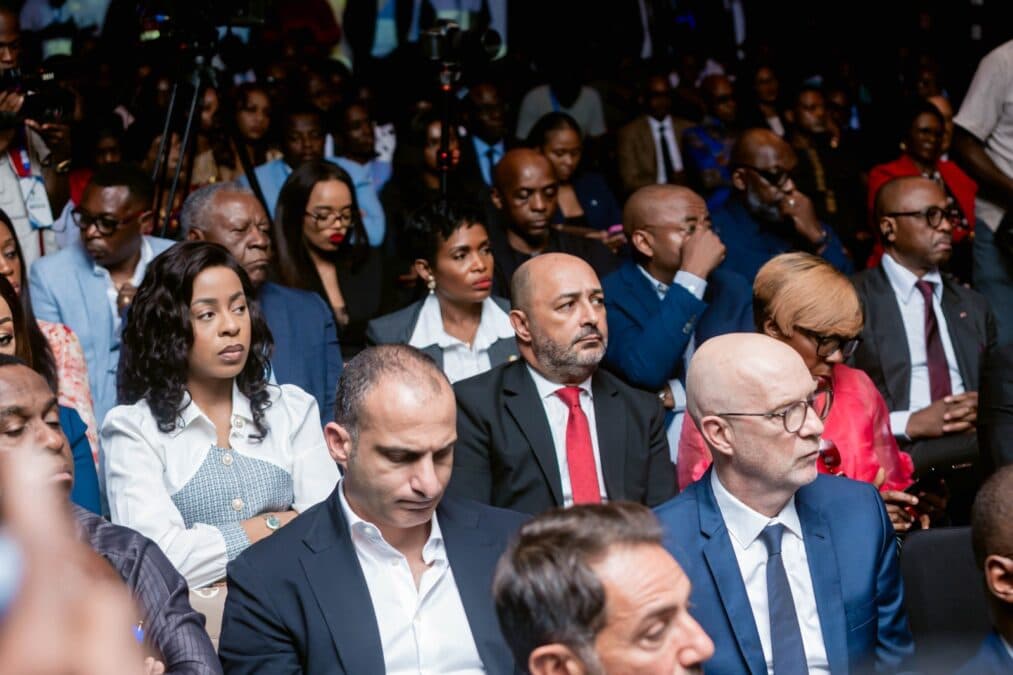 Une vue en plongée de la salle de conférence remplie d'investisseurs, d'hommes d'affaires et de partenaires attentifs aux présentations du groupe bancaire. Les participants sont installés en rangées serrées dans une ambiance professionnelle.